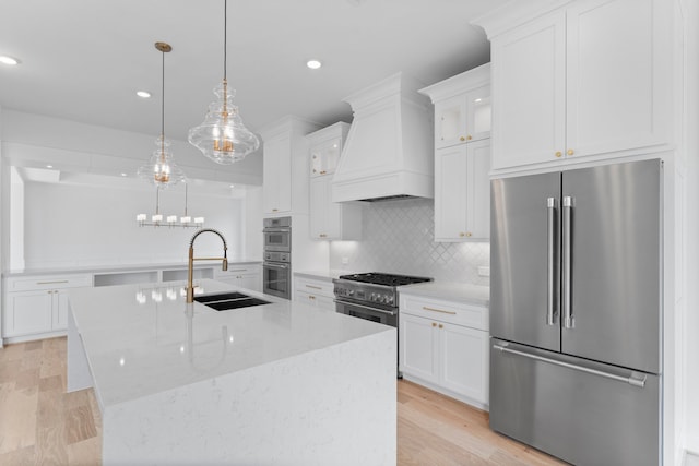 kitchen featuring stainless steel appliances, light hardwood / wood-style flooring, a center island with sink, and hanging light fixtures