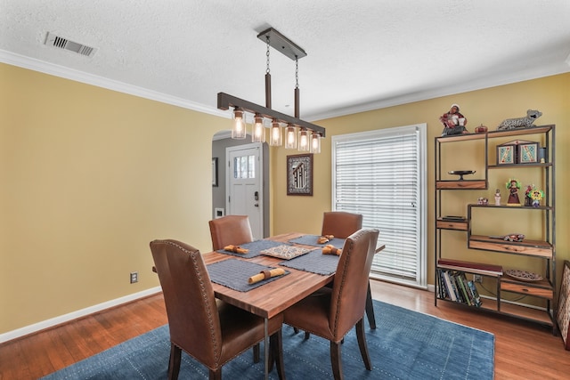 dining area with wood-type flooring, ornamental molding, and a textured ceiling