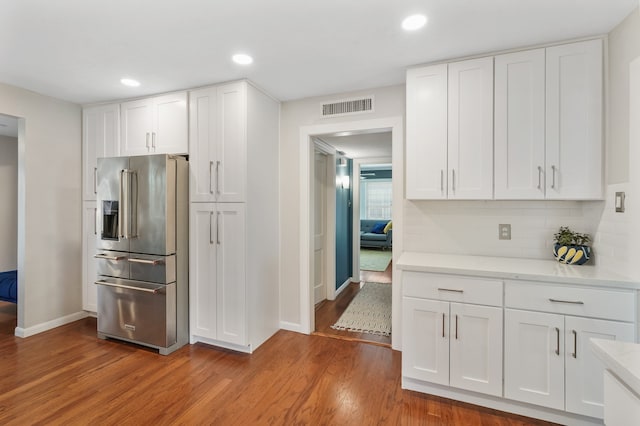 kitchen with hardwood / wood-style flooring, white cabinetry, high quality fridge, and decorative backsplash