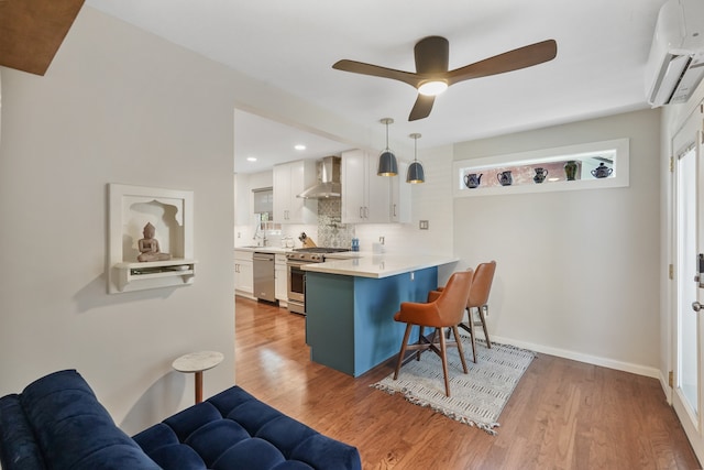 kitchen with a breakfast bar area, white cabinetry, hanging light fixtures, stainless steel appliances, and wall chimney range hood