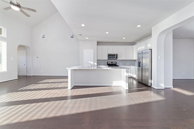 kitchen featuring a kitchen island with sink, dark hardwood / wood-style floors, stainless steel appliances, backsplash, and white cabinetry