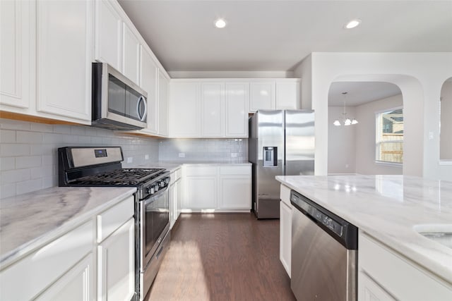 kitchen with backsplash, appliances with stainless steel finishes, white cabinetry, and dark hardwood / wood-style flooring