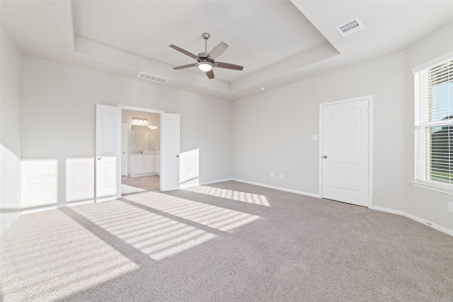 unfurnished bedroom with connected bathroom, ceiling fan, light carpet, and a raised ceiling