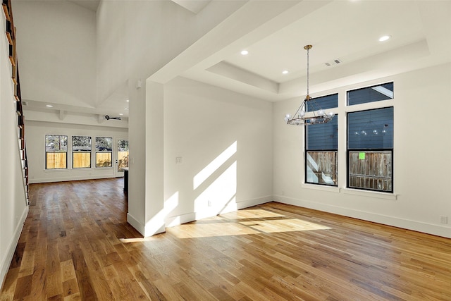 unfurnished dining area featuring hardwood / wood-style floors, a chandelier, a tray ceiling, and a high ceiling