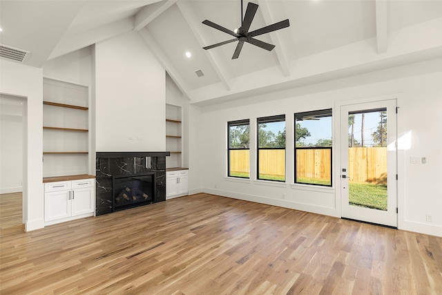 unfurnished living room with a high end fireplace, beamed ceiling, light wood-type flooring, and a wealth of natural light