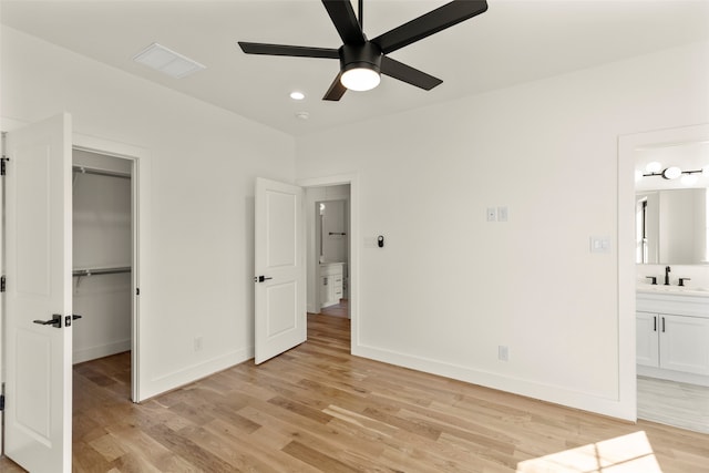 unfurnished bedroom featuring ceiling fan, light wood-type flooring, ensuite bathroom, a walk in closet, and sink