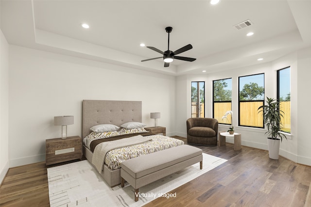 bedroom with ceiling fan, wood-type flooring, and a tray ceiling