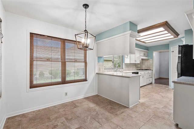 kitchen featuring black refrigerator, stainless steel gas stovetop, white cabinetry, hanging light fixtures, and kitchen peninsula