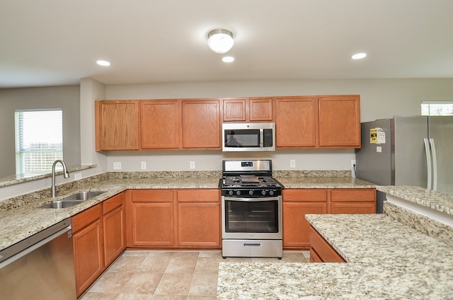 kitchen with plenty of natural light, a sink, appliances with stainless steel finishes, and light stone countertops