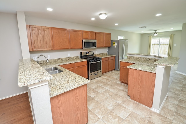 kitchen featuring kitchen peninsula, a kitchen island, light stone countertops, sink, and stainless steel appliances