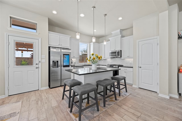 kitchen with stainless steel appliances, light hardwood / wood-style floors, white cabinetry, a kitchen bar, and hanging light fixtures