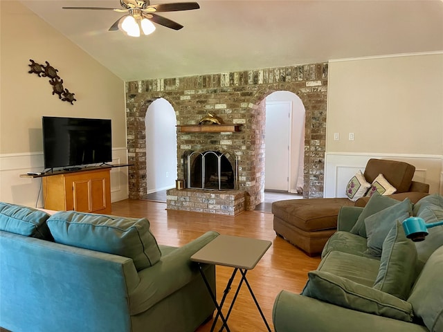 living room featuring ceiling fan, vaulted ceiling, light wood-type flooring, and a brick fireplace