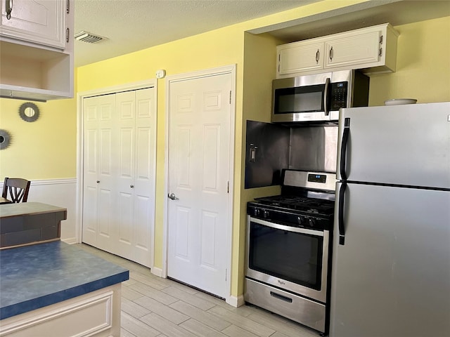 kitchen with light hardwood / wood-style flooring, white cabinets, stainless steel appliances, and a textured ceiling