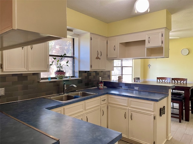 kitchen with kitchen peninsula, sink, white cabinets, light hardwood / wood-style floors, and tasteful backsplash