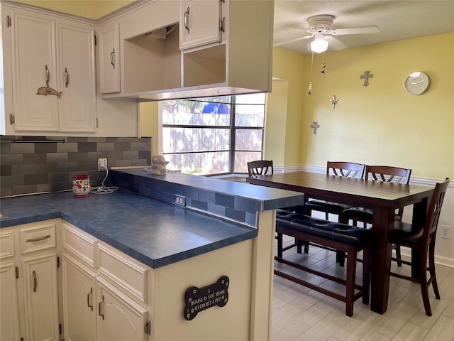 kitchen featuring light wood-type flooring, kitchen peninsula, white cabinetry, ceiling fan, and decorative backsplash