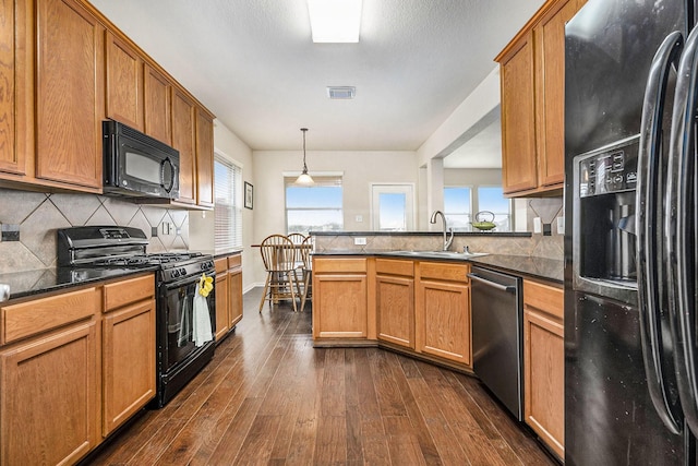 kitchen with dark stone counters, dark wood-type flooring, sink, black appliances, and hanging light fixtures