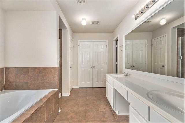 bathroom with tile patterned flooring, vanity, and tiled bath