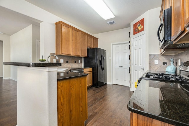 kitchen with sink, dark hardwood / wood-style flooring, kitchen peninsula, dark stone countertops, and black appliances