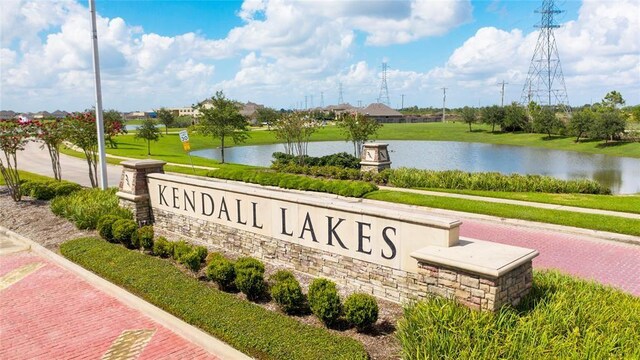 community / neighborhood sign featuring a water view and a lawn