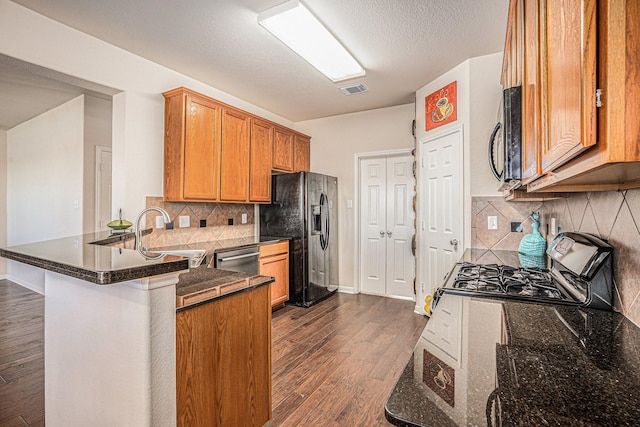 kitchen featuring black appliances, dark hardwood / wood-style floors, kitchen peninsula, and dark stone counters