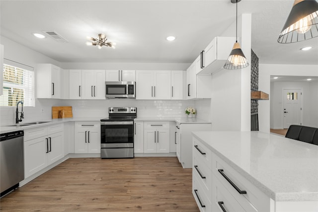 kitchen with sink, hanging light fixtures, white cabinetry, light hardwood / wood-style floors, and stainless steel appliances