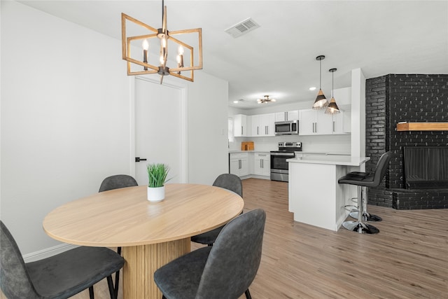 dining space featuring a notable chandelier, light hardwood / wood-style flooring, and a brick fireplace