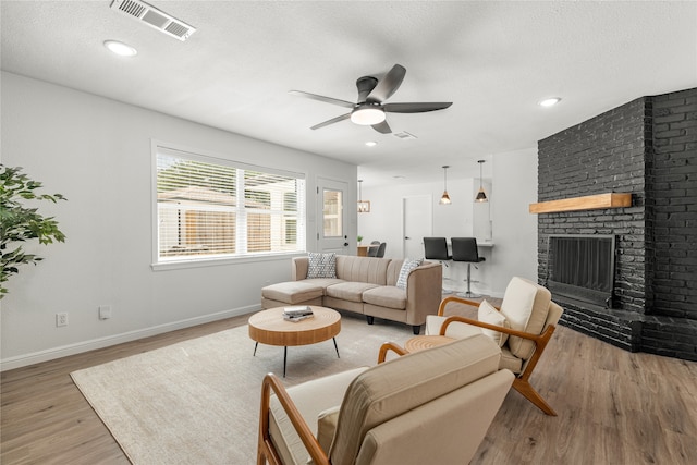 living room with a fireplace, a textured ceiling, light hardwood / wood-style floors, and ceiling fan