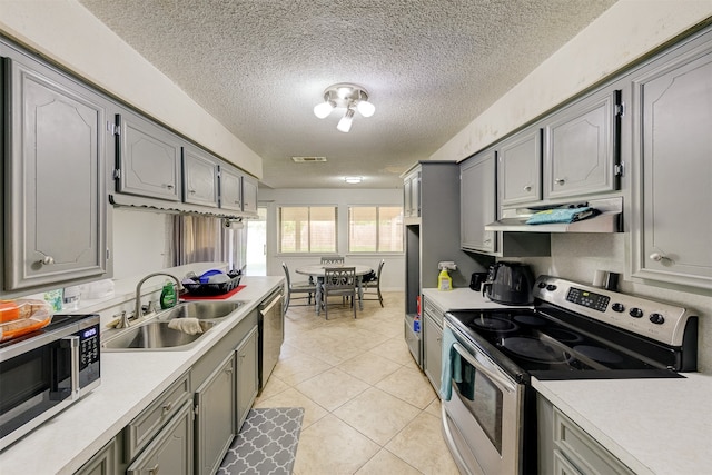 kitchen with light tile patterned floors, appliances with stainless steel finishes, a textured ceiling, gray cabinetry, and sink