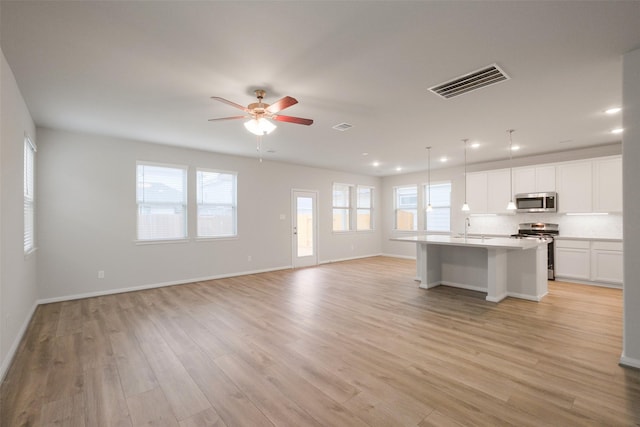 kitchen with appliances with stainless steel finishes, white cabinets, hanging light fixtures, a center island with sink, and light wood-type flooring