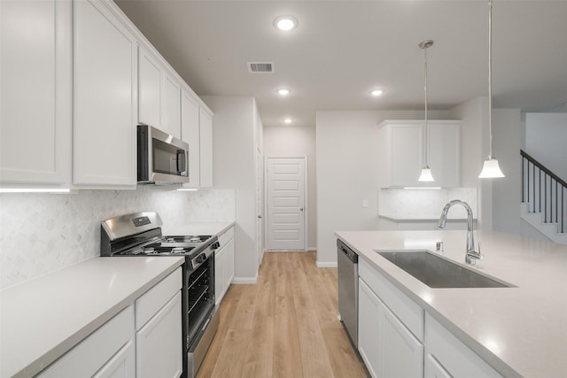 kitchen with decorative light fixtures, white cabinetry, sink, light hardwood / wood-style floors, and stainless steel appliances