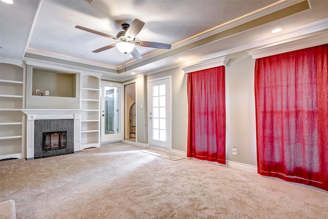 unfurnished living room with ceiling fan, a tray ceiling, ornamental molding, carpet floors, and a fireplace