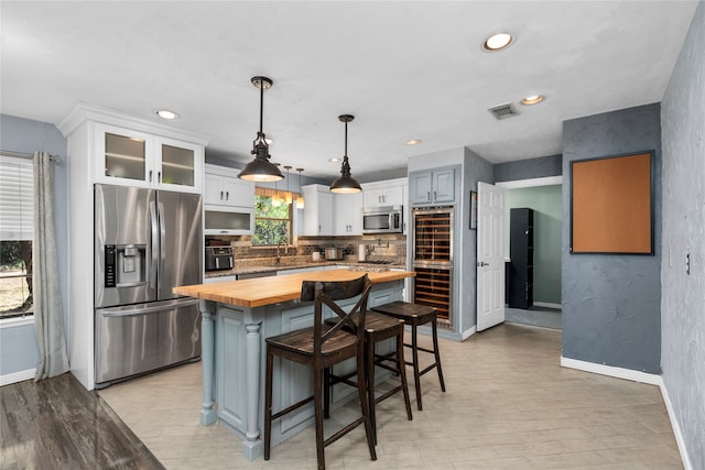 kitchen featuring wooden counters, a kitchen island, a breakfast bar area, decorative light fixtures, and appliances with stainless steel finishes