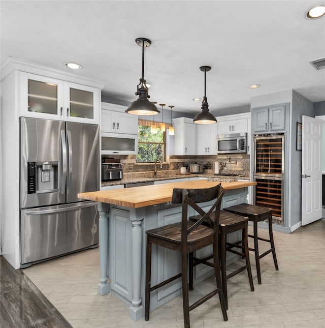 kitchen featuring white cabinets, a kitchen breakfast bar, stainless steel appliances, wooden counters, and a center island