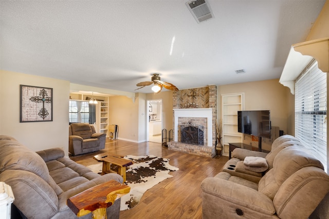 living room with hardwood / wood-style flooring, built in shelves, a textured ceiling, and a fireplace