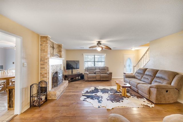 living room featuring a brick fireplace, ceiling fan, and wood-type flooring