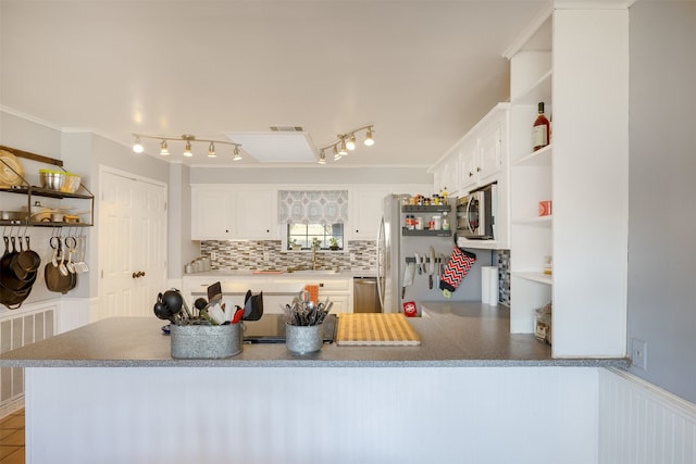 kitchen with appliances with stainless steel finishes, backsplash, white cabinetry, kitchen peninsula, and ornamental molding