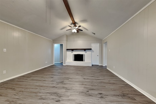 unfurnished living room featuring vaulted ceiling with beams, a fireplace, ceiling fan, crown molding, and hardwood / wood-style flooring