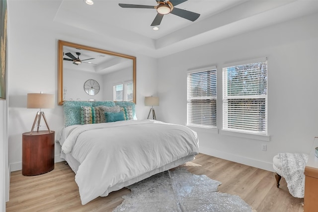 bedroom with ceiling fan, a raised ceiling, and light wood-type flooring