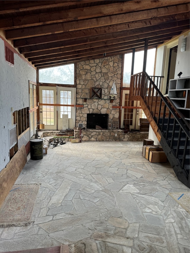 living room featuring a wealth of natural light, lofted ceiling with beams, and a stone fireplace