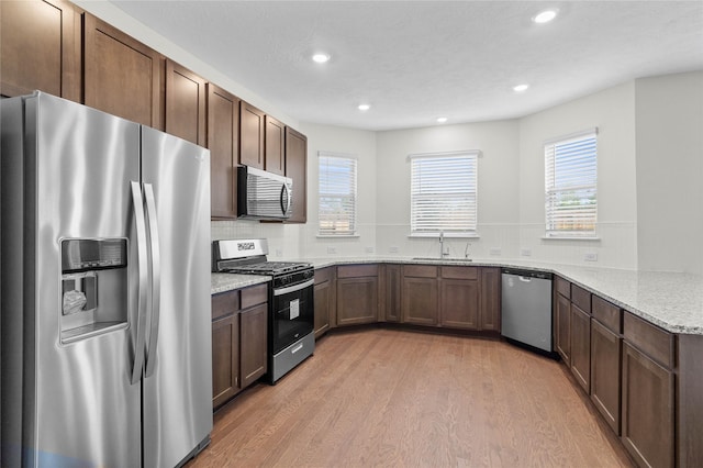 kitchen with light stone countertops, a wealth of natural light, stainless steel appliances, and light wood-type flooring