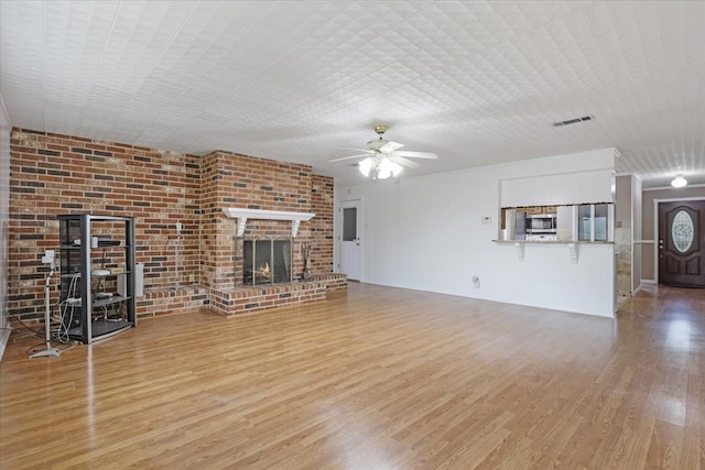 unfurnished living room with brick wall, a fireplace, wood-type flooring, and ceiling fan