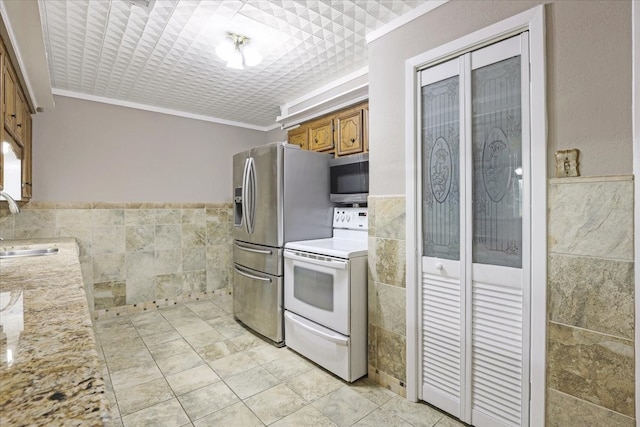 kitchen with stainless steel appliances, ornamental molding, sink, tile walls, and light stone counters