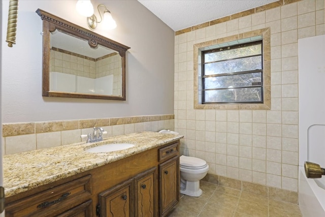 bathroom featuring a textured ceiling, toilet, tile walls, vanity, and tile patterned flooring