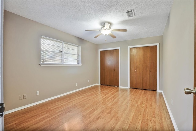 unfurnished bedroom featuring light hardwood / wood-style floors, a textured ceiling, multiple closets, and ceiling fan