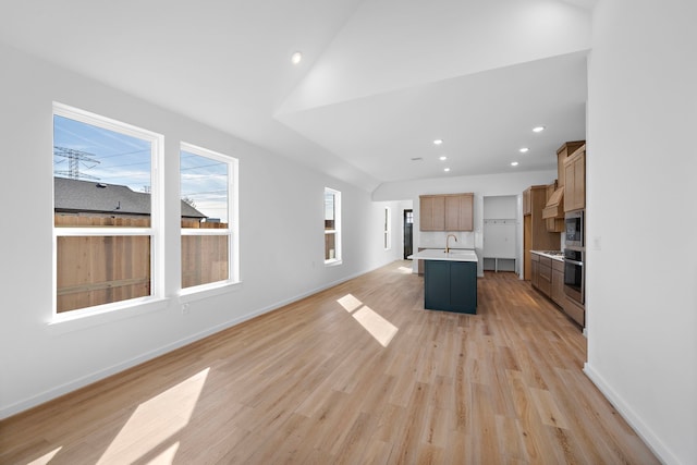 kitchen featuring stainless steel oven, a breakfast bar area, a center island with sink, and light hardwood / wood-style flooring