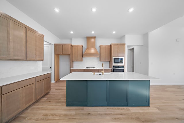 kitchen with premium range hood, appliances with stainless steel finishes, sink, and a center island with sink