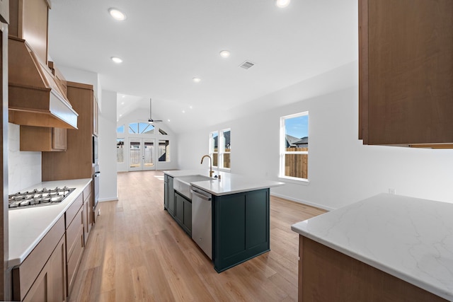 kitchen featuring vaulted ceiling, appliances with stainless steel finishes, sink, light hardwood / wood-style floors, and a center island with sink