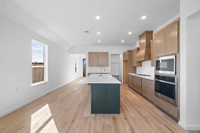 kitchen featuring sink, decorative backsplash, light hardwood / wood-style floors, stainless steel appliances, and a center island with sink