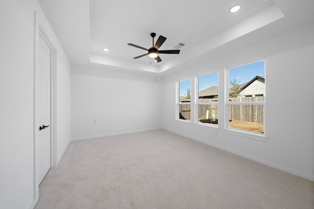 unfurnished room with ceiling fan, a raised ceiling, and light carpet