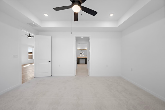 unfurnished bedroom with ceiling fan, a tray ceiling, and light carpet